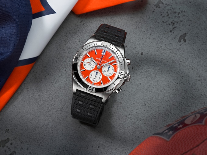 The Chronomat B01 42 NFL Denver Broncos Edition with a bright orange dial next to a jersey.